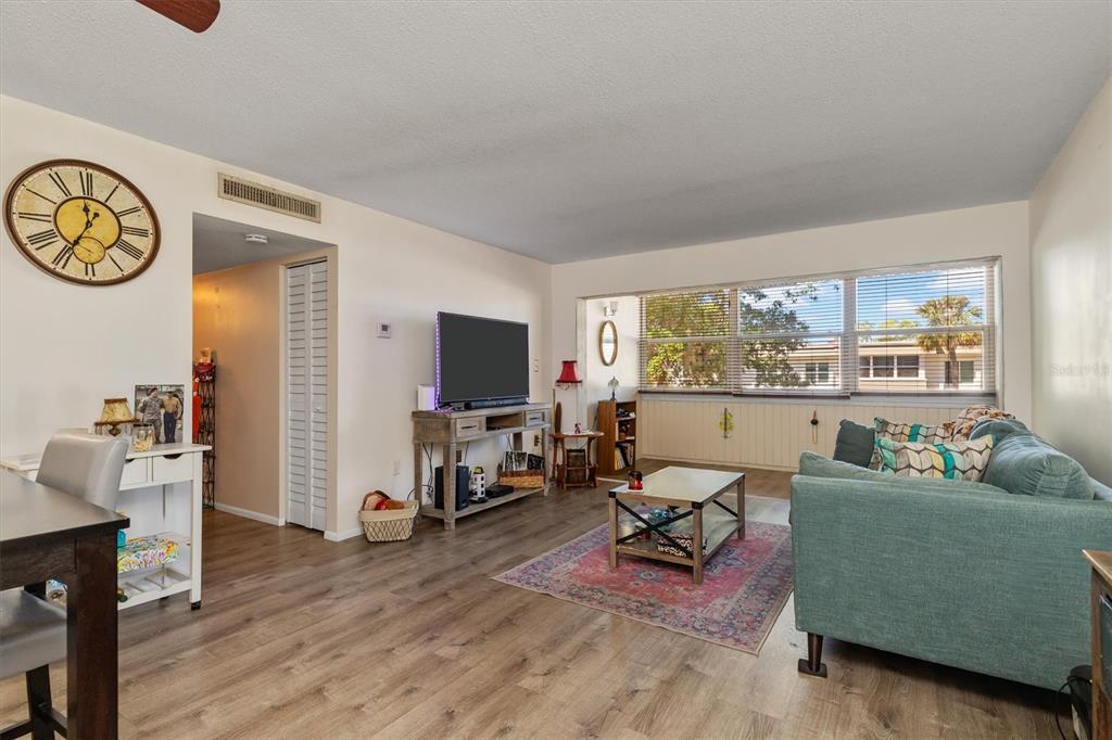A living room features wood-look flooring, a teal sofa, a television console, and large windows — 2437 HARBOR BOULEVARD UNIT 204, PORT CHARLOTTE, FL
