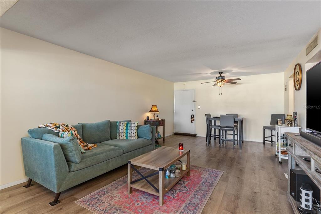 A living room with a teal sofa, wood coffee table, and dining area on wood flooring — 2437 HARBOR BOULEVARD UNIT 204, PORT CHARLOTTE, FL