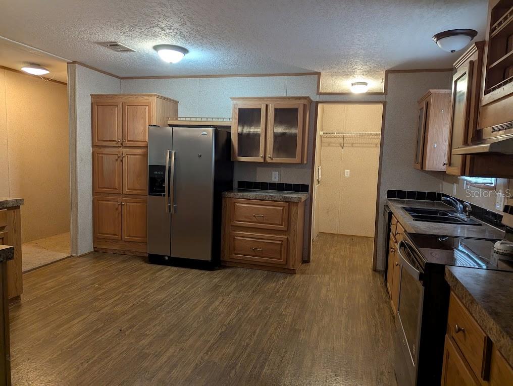 A kitchen with wood cabinets, stainless steel appliances, and dark countertops on wood-look flooring — 15319 SW 114TH PLACE, ARCHER, FL