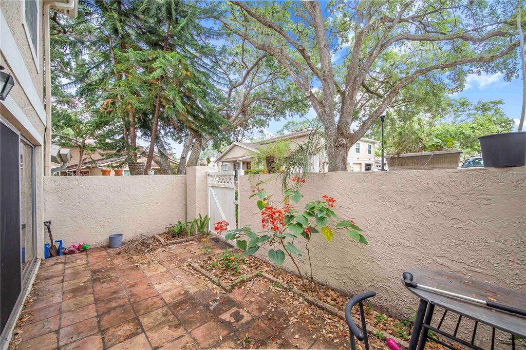 A small, tiled patio features a stucco wall, a white gate, and a flowering plant — 11857 NORTHTRAIL AVENUE, TEMPLE TERRACE, FL