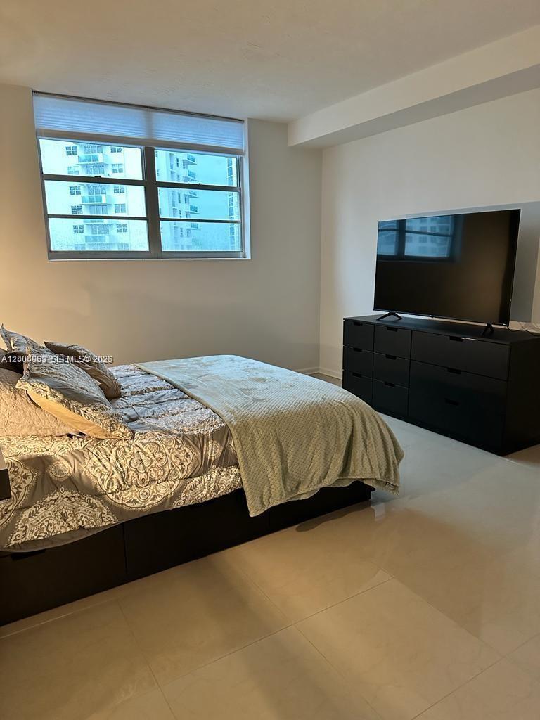 A bedroom features a bed, a black dresser with a television, and a large window — 3000 S Ocean Dr # 414, Hollywood FL 33019, HOLLYWOOD, FL