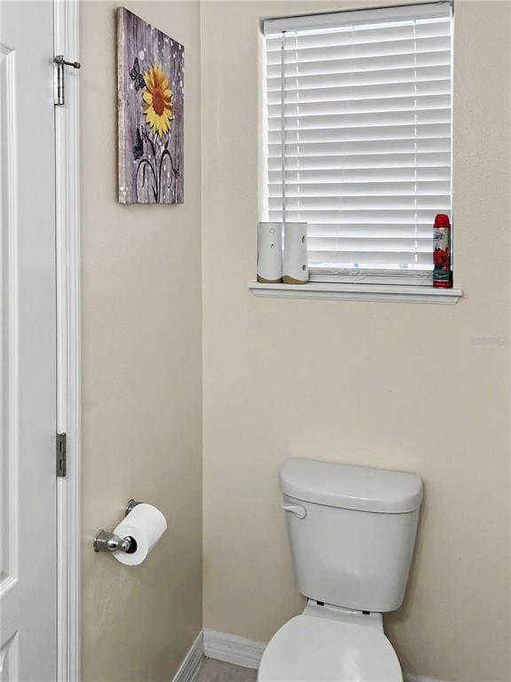 A bathroom features a toilet, a window with white blinds, and a sunflower wall art — 2239 CANYON BREEZE AVENUE, KISSIMMEE, FL