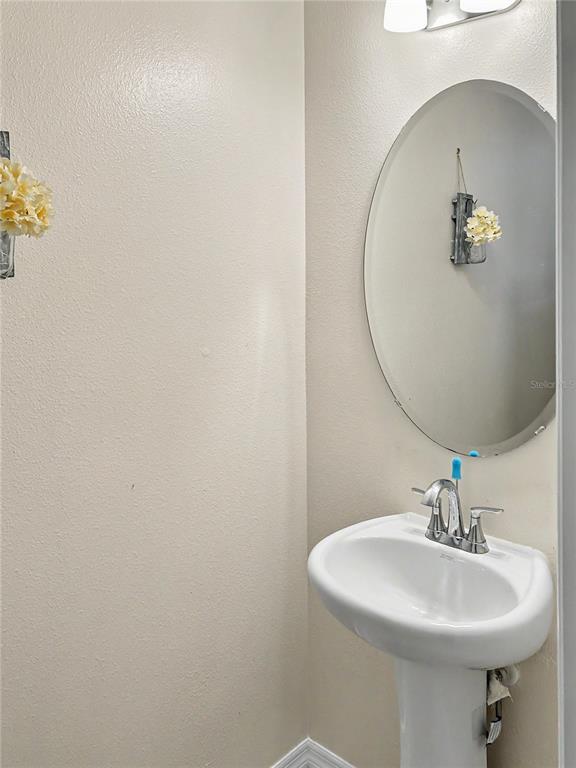 A small bathroom features a white pedestal sink, an oval mirror, and beige walls — 2239 CANYON BREEZE AVENUE, KISSIMMEE, FL