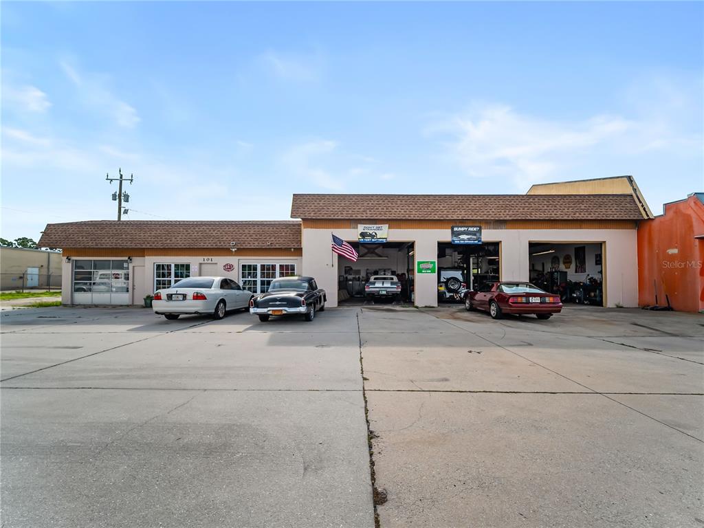 An exterior view of an automotive repair shop with three garage bays and parked cars — 101 S INDIANA AVENUE, ENGLEWOOD, FL