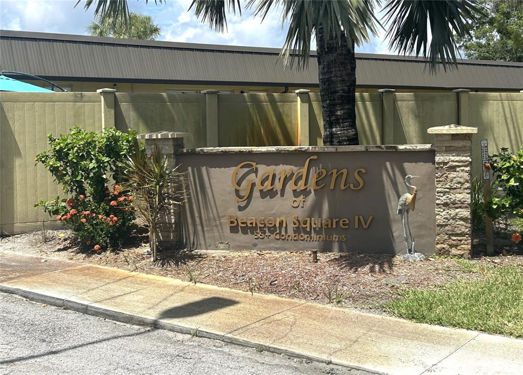 A sign for Gardens of Beacon Square IV stands in front of a tan fence — 4211 STRATFORD DRIVE UNIT 4211, NEW PORT RICHEY, FL