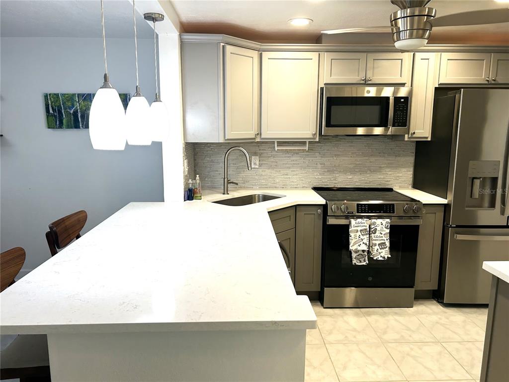 A kitchen features white countertops, gray cabinetry, stainless steel appliances, and three pendant lights — 4211 STRATFORD DRIVE UNIT 4211, NEW PORT RICHEY, FL