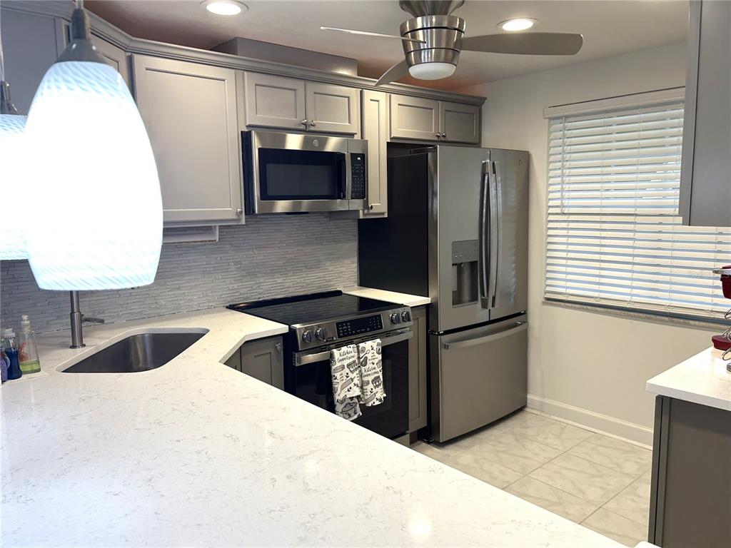 A kitchen features gray cabinets, stainless steel appliances, and white quartz countertops — 4211 STRATFORD DRIVE UNIT 4211, NEW PORT RICHEY, FL