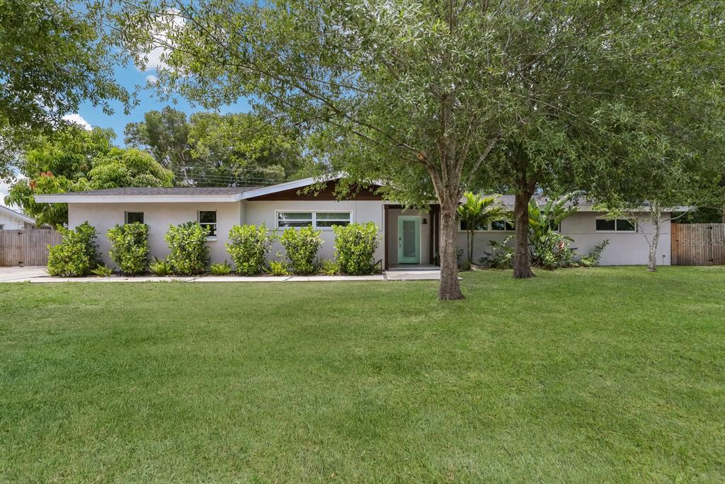 A single-story house with a light-colored exterior, a teal front door, and a large lawn — 5720 ISANDA PLACE, SARASOTA, FL