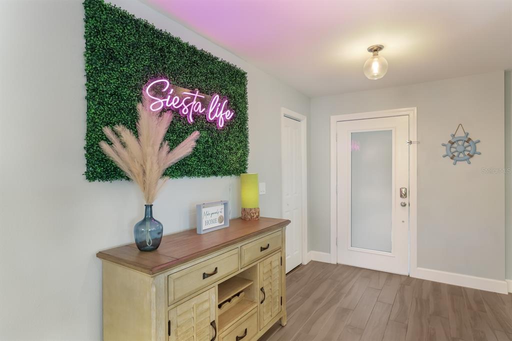 An entryway features a wood console table, a neon sign on a green wall, and flooring — 5720 ISANDA PLACE, SARASOTA, FL