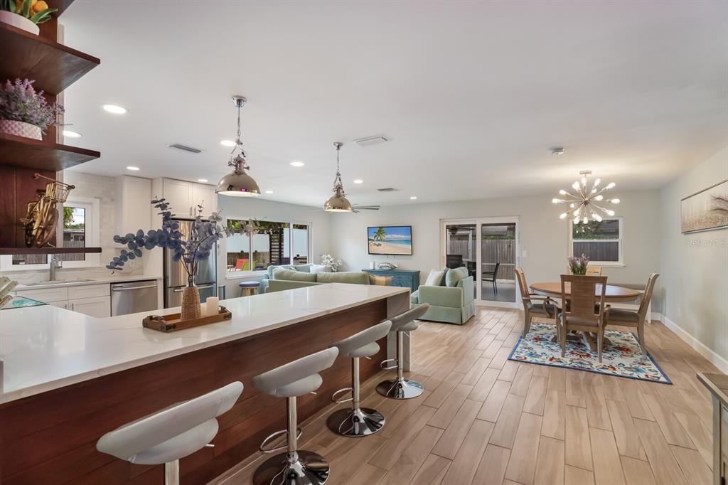 An open-concept kitchen and dining area features a white quartz island, bar stools, and tile flooring — 5720 ISANDA PLACE, SARASOTA, FL
