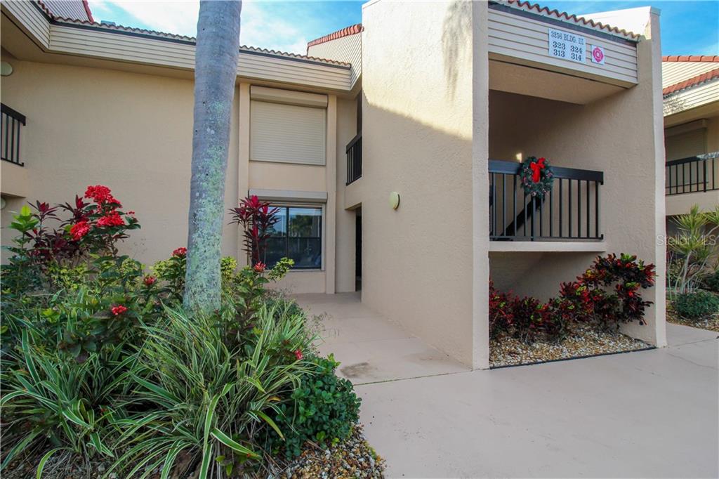 A two-story tan stucco apartment building features a covered entryway, balcony, and landscaped garden — 3256 WHITE IBIS COURT UNIT 27, PUNTA GORDA, FL