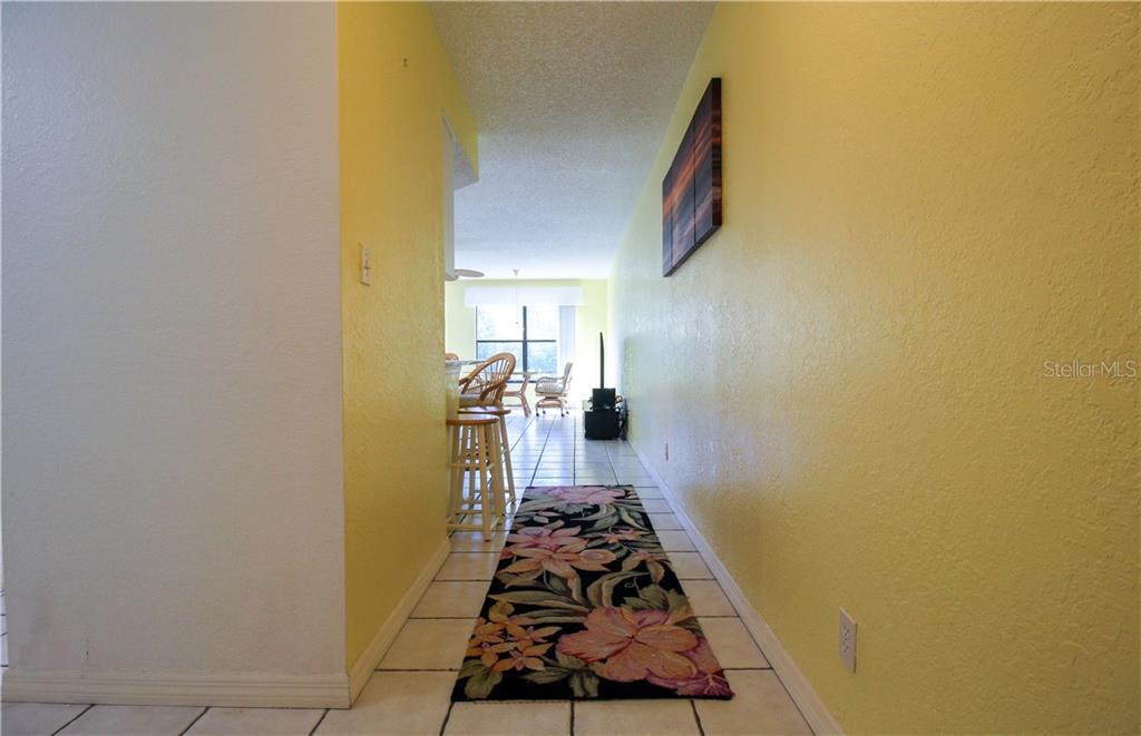 A hallway with yellow walls, tile flooring, and a floral runner leads to a dining area — 3256 WHITE IBIS COURT UNIT 27, PUNTA GORDA, FL