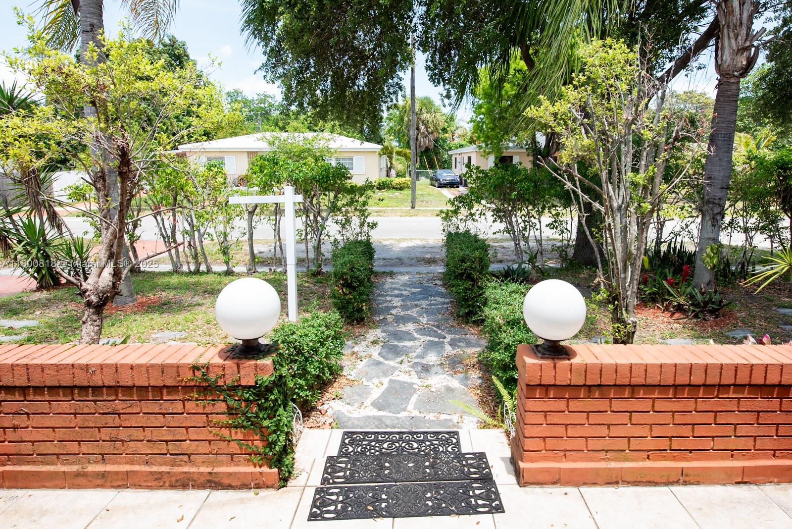 A brick wall with two globe lights frames a stone walkway leading to a street — 16910 NE 8th Ct, North Miami Beach FL 33162, NORTH MIAMI BEACH, FL
