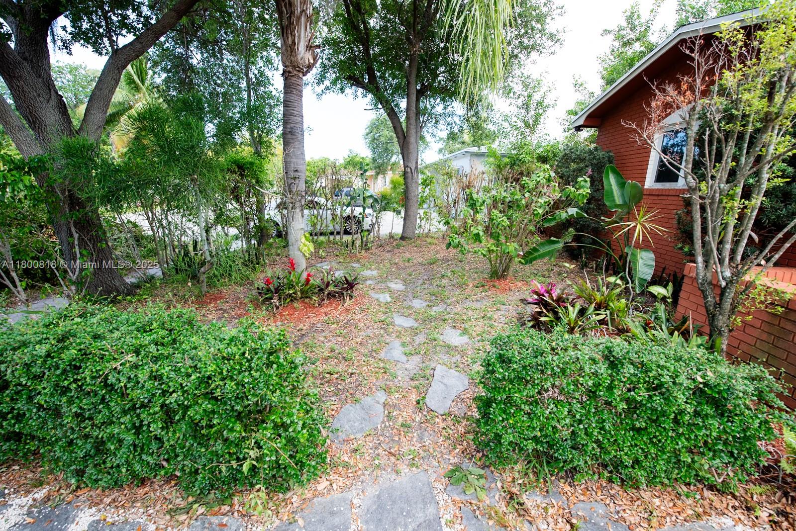A stone path leads through a landscaped yard toward a red brick house exterior — 16910 NE 8th Ct, North Miami Beach FL 33162, NORTH MIAMI BEACH, FL