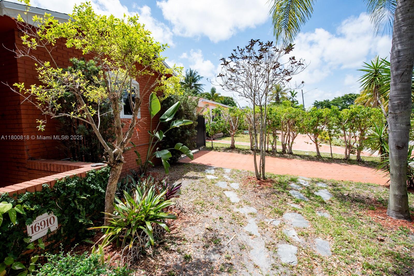 A brick house exterior features a stone walkway, landscaping, and a visible address number — 16910 NE 8th Ct, North Miami Beach FL 33162, NORTH MIAMI BEACH, FL