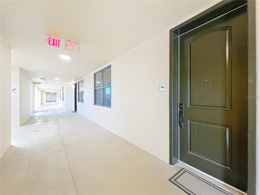 A dark door labeled 306 opens onto a long, brightly lit apartment building hallway — 16300 COUNTY ROAD 455 UNIT 306, MONTVERDE, FL