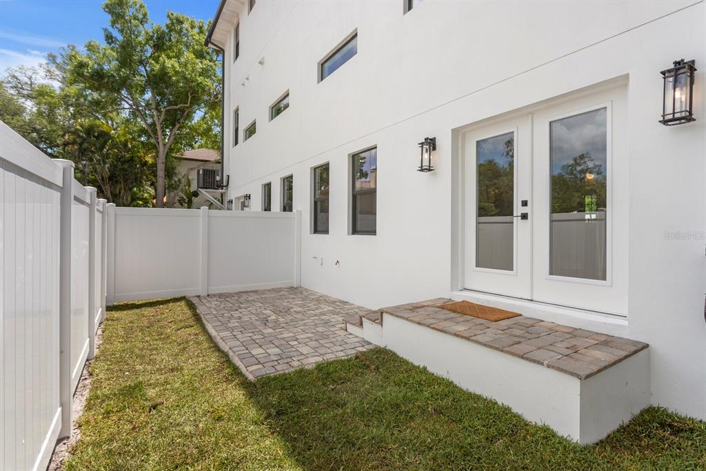 A white exterior wall features a paved patio, a small stoop, and double glass doors — 5210 BAYSHORE BOULEVARD UNIT 3, TAMPA, FL