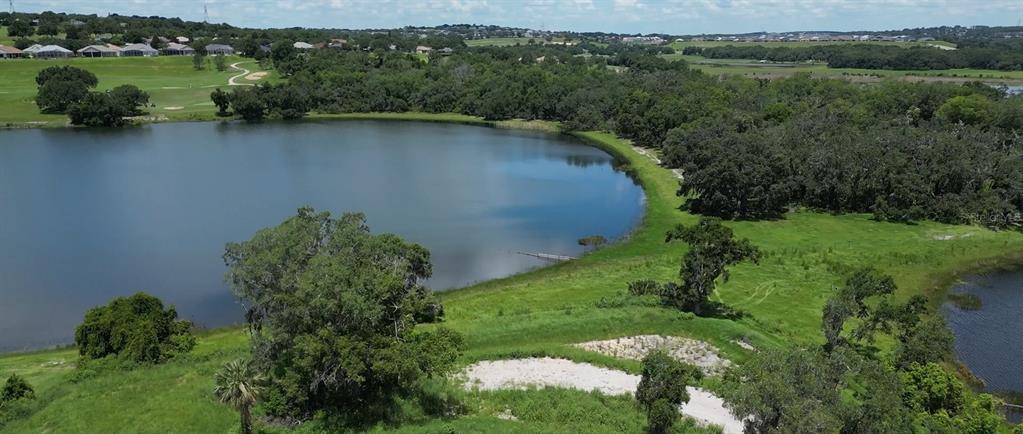 An aerial view shows a large lake surrounded by green fields, trees, and distant houses — 133 TRANQUIL MIRROR LAKE COURT Lot 16, CLERMONT, FL