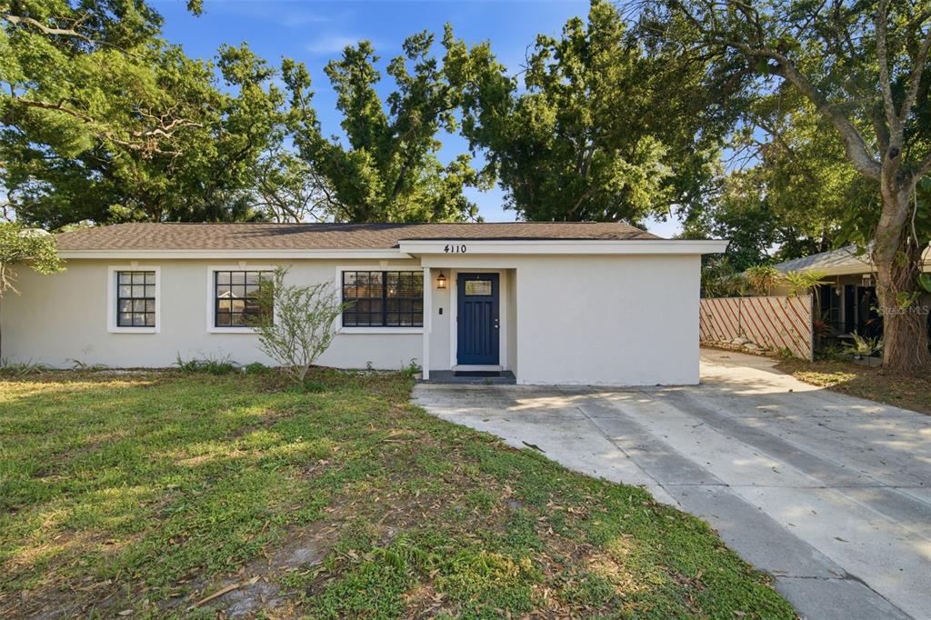 A single-story house with a blue front door, concrete driveway, and large trees in front — 4110 W LEILA AVENUE, TAMPA, FL