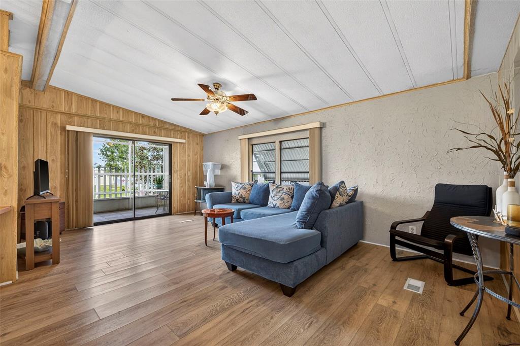 A living room features wood-look flooring, a blue sectional sofa, and a sliding glass door — 7880 54TH AVENUE N UNIT 38, ST PETERSBURG, FL