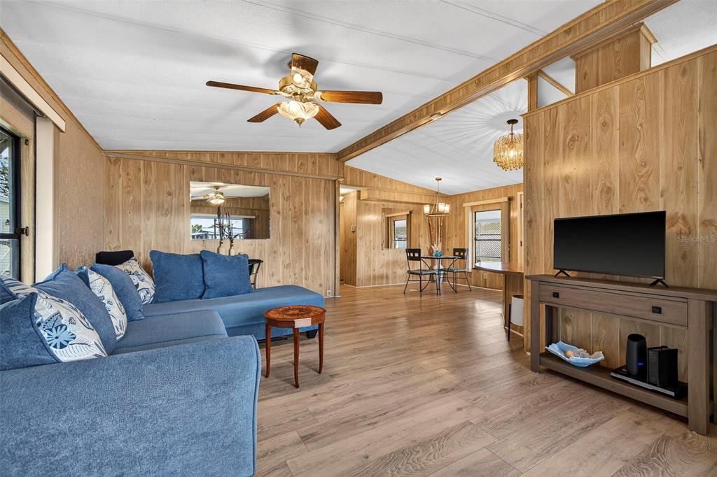 A living room with wood-paneled walls, a blue sectional sofa, and light wood-look flooring — 7880 54TH AVENUE N UNIT 38, ST PETERSBURG, FL