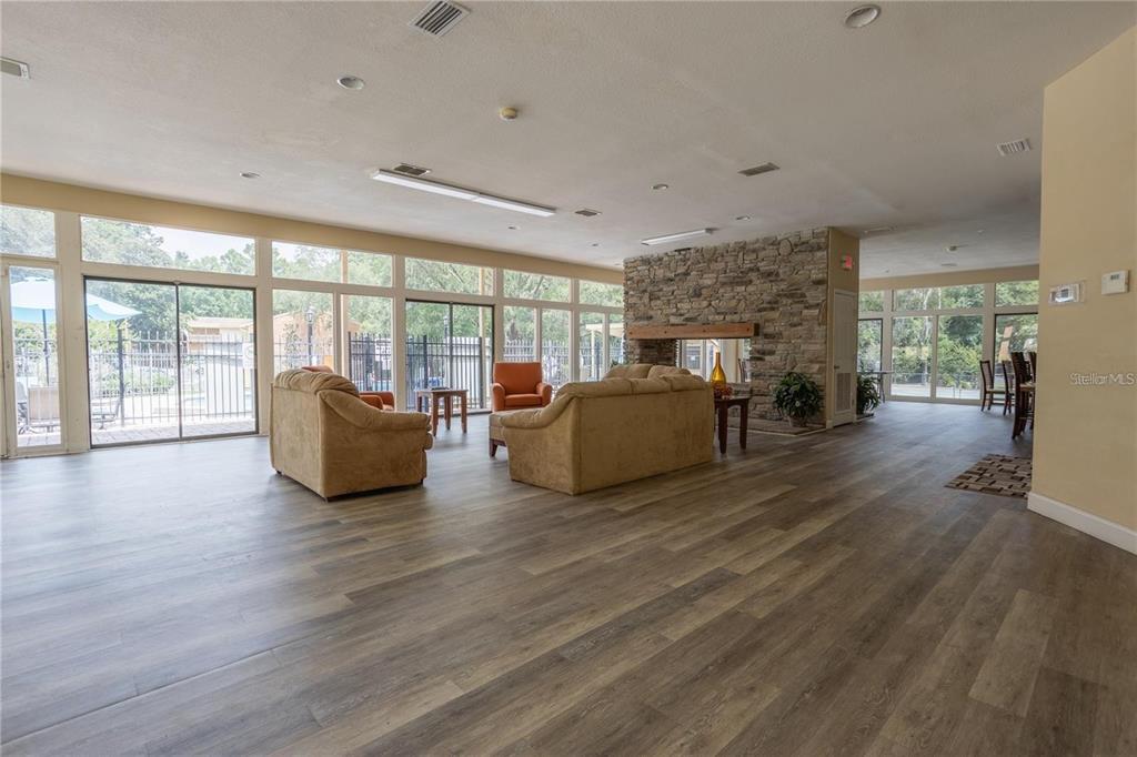 A spacious room with wood-look flooring, a stone fireplace, and large windows overlooking a pool — 1810 NW 23RD BOULEVARD UNIT 202, GAINESVILLE, FL