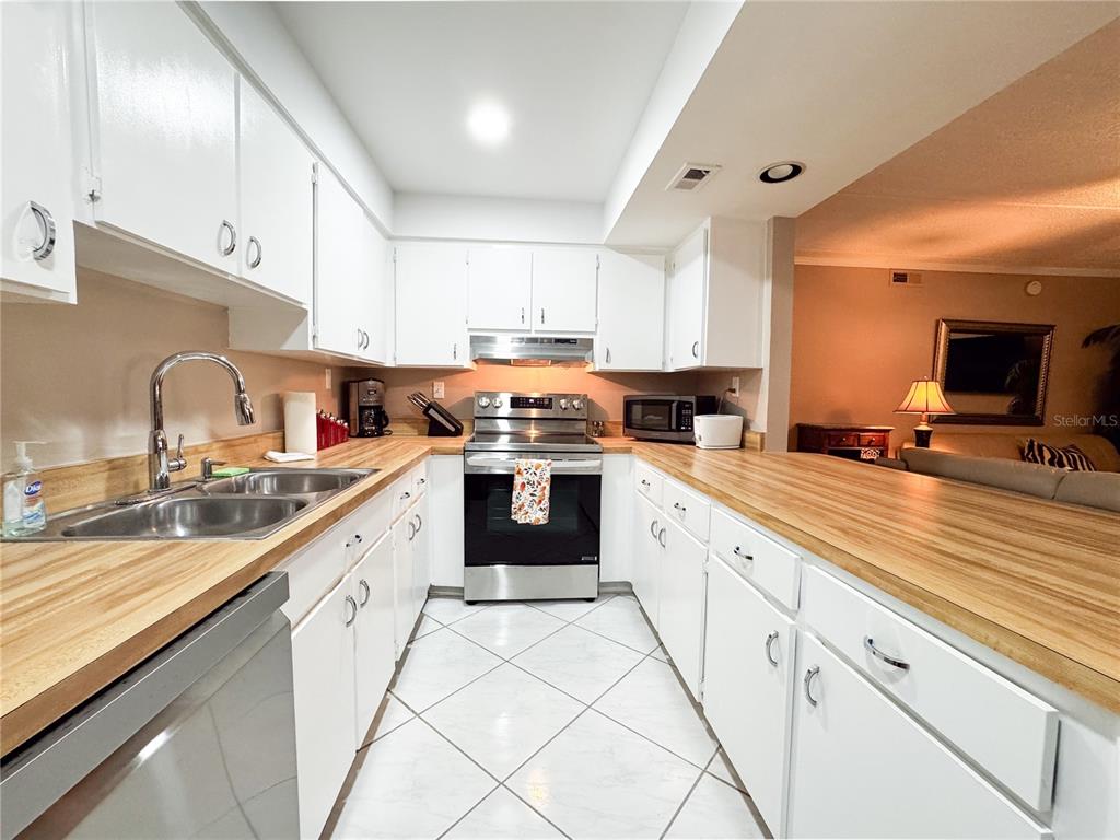 A galley kitchen features white cabinets, light wood countertops, stainless steel appliances, and tile flooring — 12760 INDIAN ROCKS ROAD UNIT 510, LARGO, FL