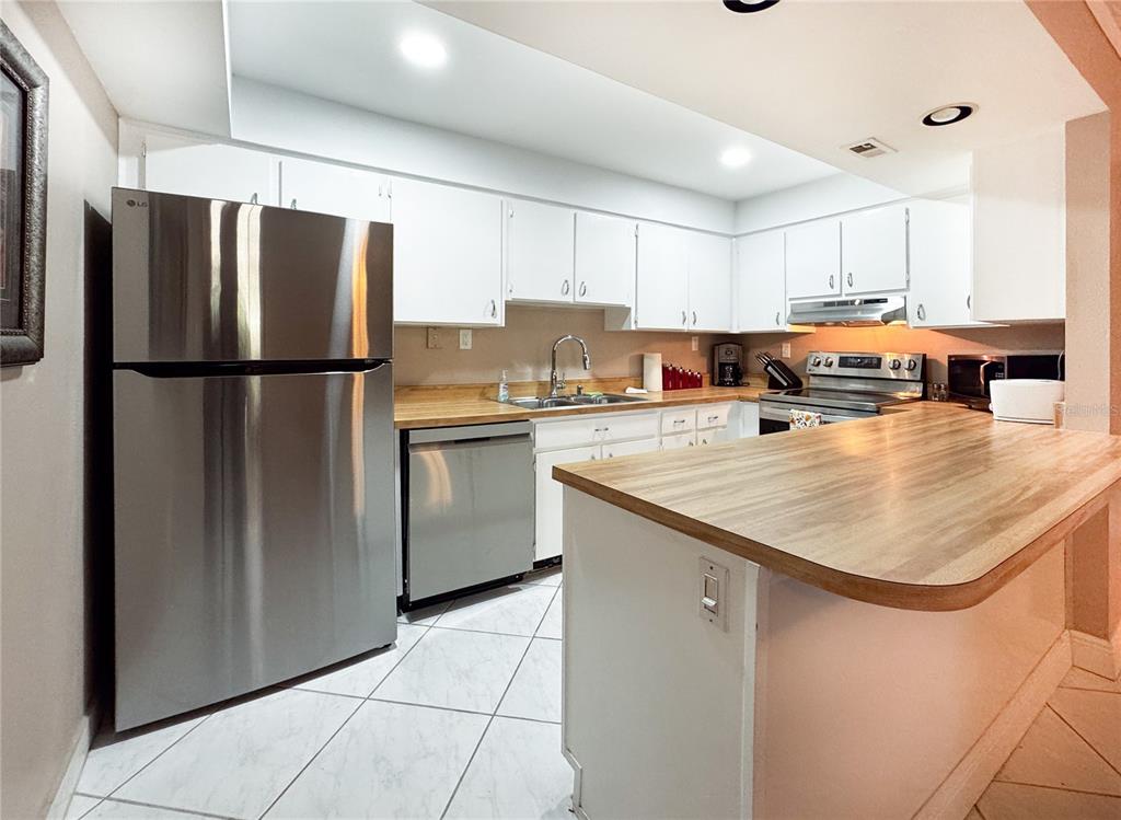 A kitchen features white cabinets, stainless steel appliances, and a wood-look countertop peninsula — 12760 INDIAN ROCKS ROAD UNIT 510, LARGO, FL