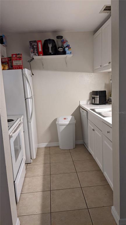 A small kitchen features white cabinets, white appliances, tile flooring, and a trash can — 4000 SW 23RD STREET UNIT 3-107, GAINESVILLE, FL