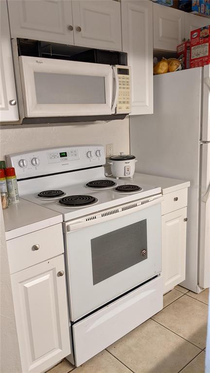 A kitchen features white cabinets, a white electric stove, a microwave, and a white refrigerator — 4000 SW 23RD STREET UNIT 3-107, GAINESVILLE, FL