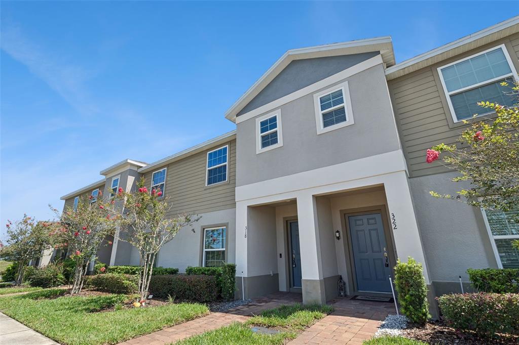 A two-story townhouse exterior features gray stucco, tan siding, and two blue front doors — 318 ANNABELLE WAY, DAVENPORT, FL