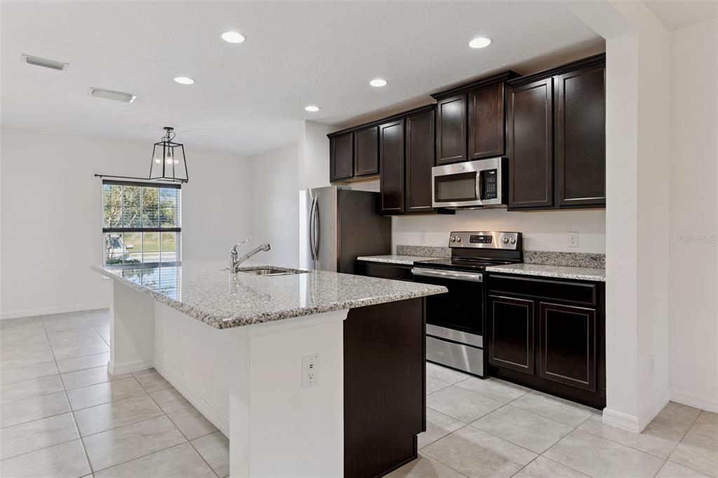 A kitchen with dark wood cabinets, granite countertops, stainless steel appliances, and a center island — 318 ANNABELLE WAY, DAVENPORT, FL