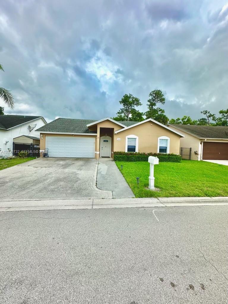 A single-story suburban house features a two-car garage, tan stucco siding, and a front lawn — 1010 Salmon Isle, Green Acres FL 33413, GREEN ACRES, FL