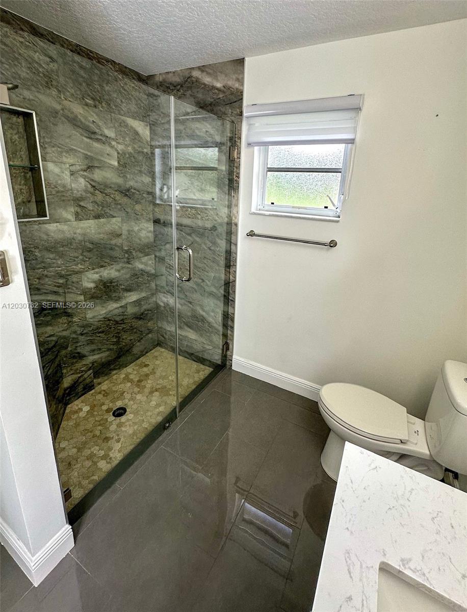 A bathroom features a glass-enclosed shower with stone-look tile, a toilet, and dark floor tiles — 1010 Salmon Isle, Green Acres FL 33413, GREEN ACRES, FL