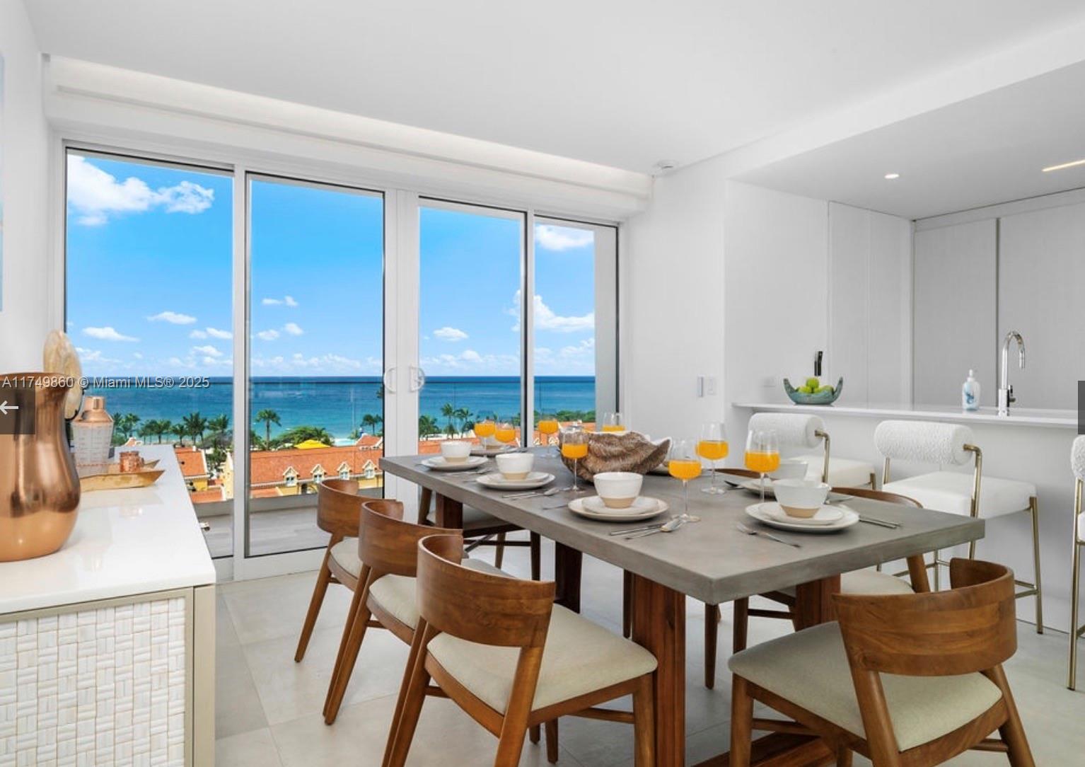 A dining room with a concrete table, wooden chairs, and floor-to-ceiling windows overlooking the ocean — 1 NW IRAUSQUIN BLV # 1A, Au, Au