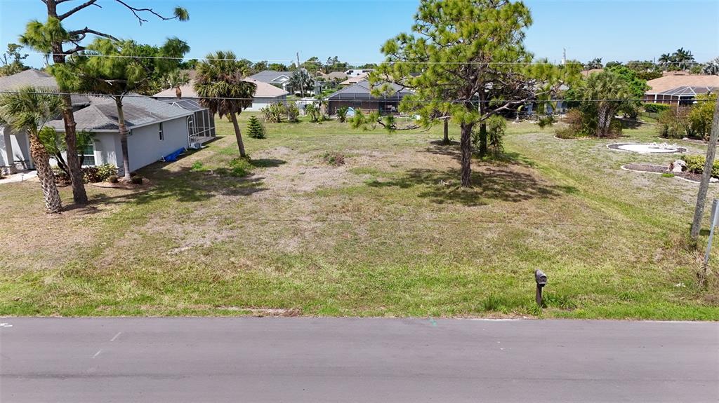 An elevated view of a vacant, grassy residential lot bordered by trees and neighboring houses — 9 LONG MEADOW LANE, ROTONDA WEST, FL