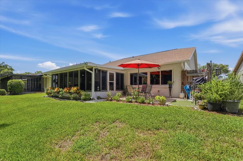 A backyard view of a house with a screened-in porch, patio, and red umbrella — 11602 WHITE ASH DRIVE, NEW PORT RICHEY, FL