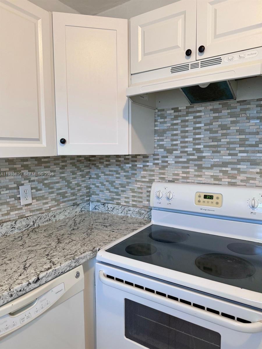 A kitchen features white cabinets, granite countertops, a tiled backsplash, and a white electric range — 269 Brittany # F, Delray Beach FL 33446, DELRAY BEACH, FL