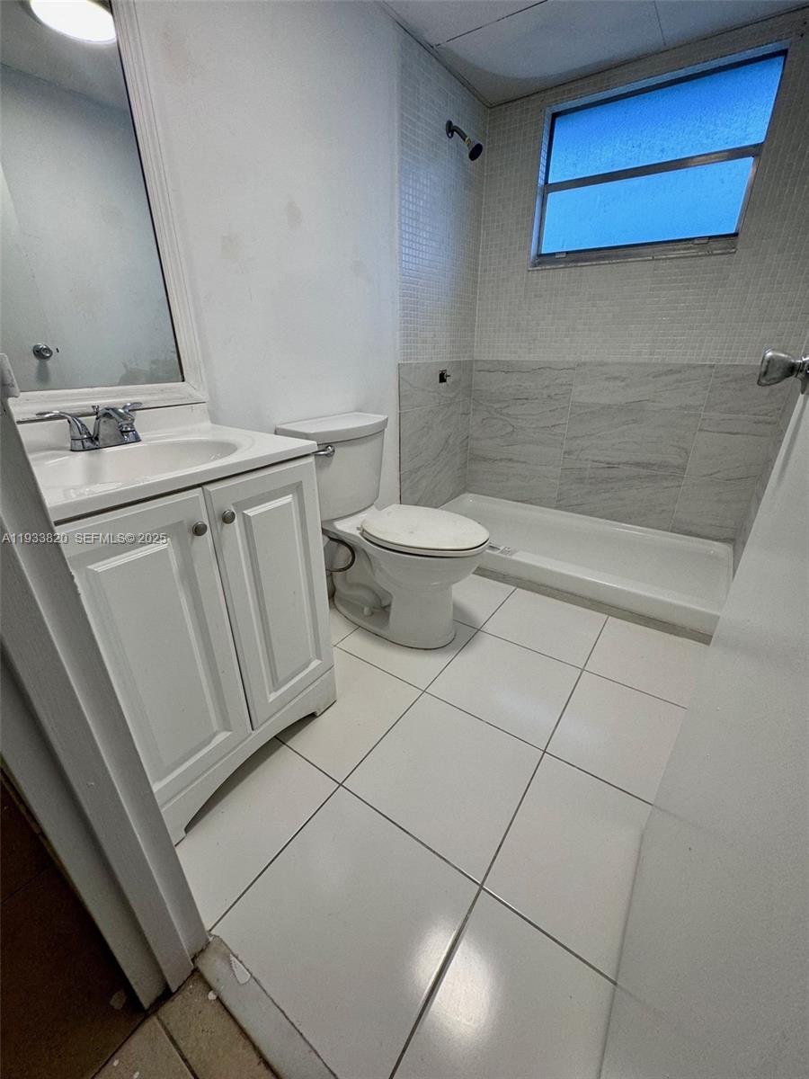 A bathroom features a white vanity, a toilet, and a tiled walk-in shower — 269 Brittany # F, Delray Beach FL 33446, DELRAY BEACH, FL