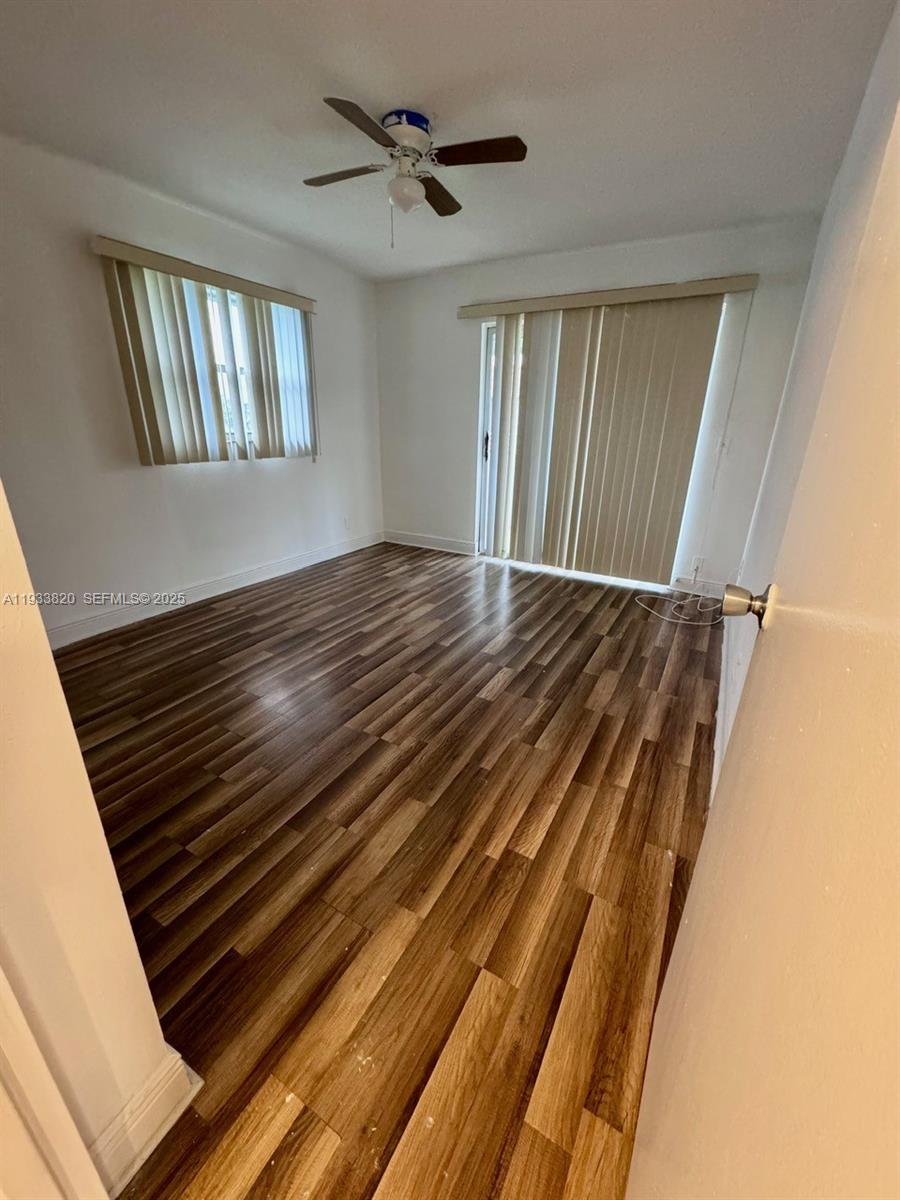 An empty room features wood-look laminate flooring, a ceiling fan, and vertical window blinds — 269 Brittany # F, Delray Beach FL 33446, DELRAY BEACH, FL