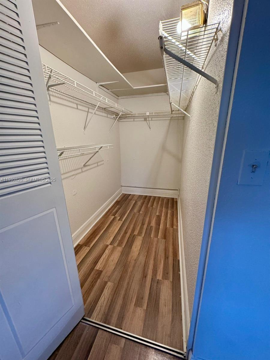 A walk-in closet features white wire shelving, light-colored walls, and wood-look flooring — 269 Brittany # F, Delray Beach FL 33446, DELRAY BEACH, FL