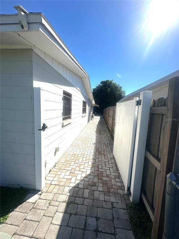A paved walkway runs between a white exterior wall and a wooden fence — 821 THALIA DRIVE, ORLANDO, FL