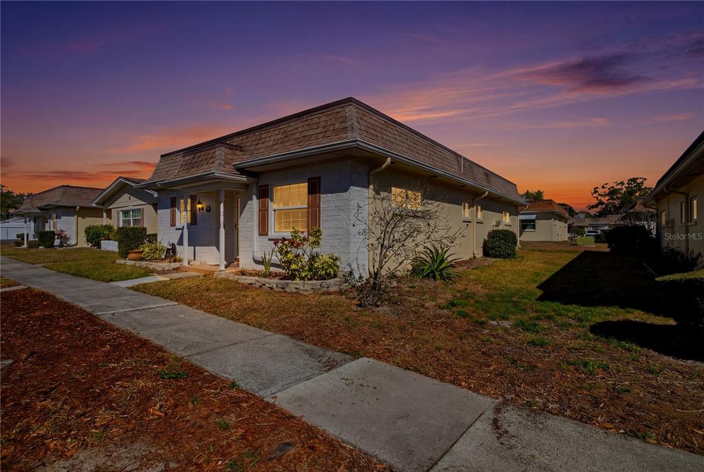 A single-story house with a mansard roof and white brick exterior at sunset — 1636 S LAKE AVENUE UNIT 1, CLEARWATER, FL