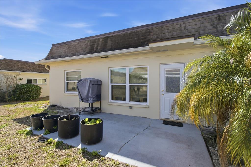 A concrete patio sits outside a beige house with a grill and several potted plants — 1636 S LAKE AVENUE UNIT 1, CLEARWATER, FL