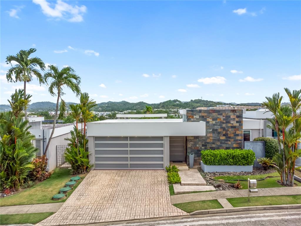 A modern single-story house features a stone facade, a gray garage door, and palm trees — 236 REY FERNANDO, GUAYNABO, PR