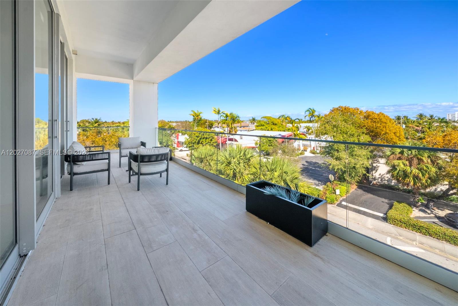 A balcony features light-colored wood-look tile flooring, modern outdoor seating, and a glass railing — 246 NE 6th Ave # 302, Delray Beach FL 33483, DELRAY BEACH, FL