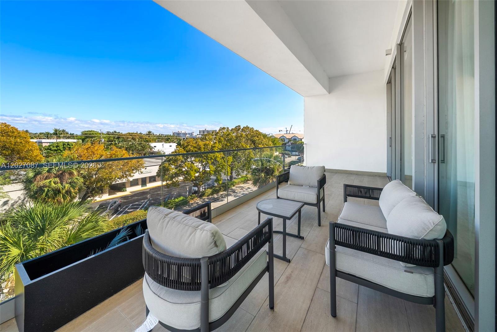 A balcony with modern patio furniture overlooks a street lined with trees and buildings — 246 NE 6th Ave # 302, Delray Beach FL 33483, DELRAY BEACH, FL