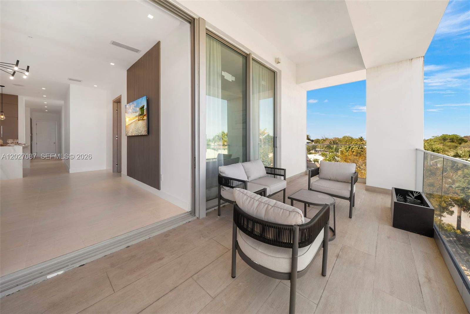 A modern balcony with outdoor seating overlooks a sunny landscape next to an indoor living area — 246 NE 6th Ave # 302, Delray Beach FL 33483, DELRAY BEACH, FL