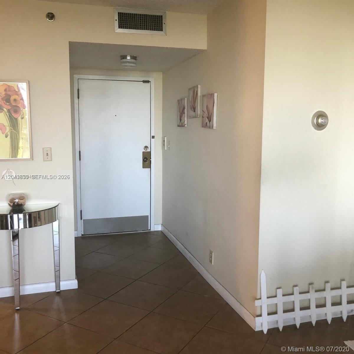 An entryway features a white door, tiled floors, a mirrored console table, and wall art — 2000 Towerside Ter # 905, Miami FL 33138, MIAMI, FL