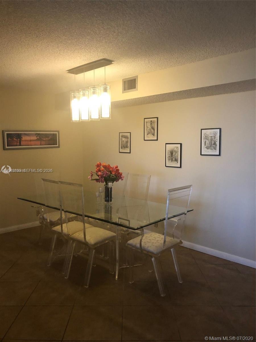 A dining room features a glass-top table with acrylic chairs and a modern pendant light — 2000 Towerside Ter # 905, Miami FL 33138, MIAMI, FL